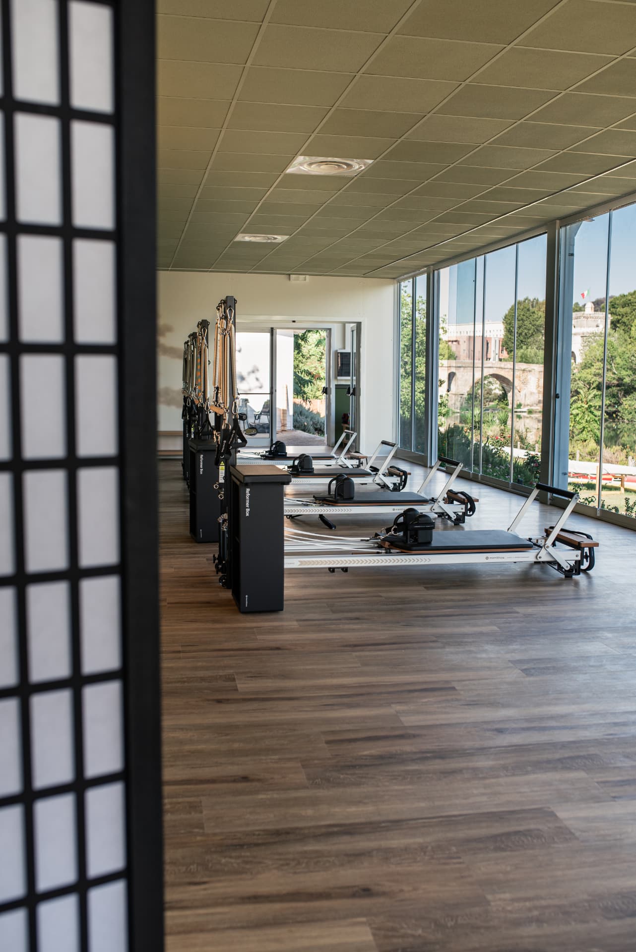 Uptown Studio Pilates room with Reformers facing floor-to-ceiling windows overlooking Ponte Milvio and the Tiber